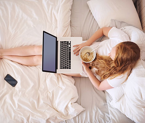 Woman having breakfast in bed while using computer