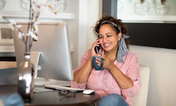woman talks on the phone while working on the computer and drinking coffee