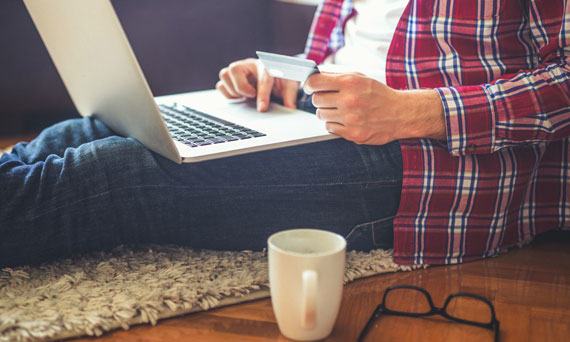 person uses laptop while drinking coffee and holding a debit card