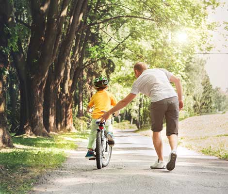 father teaches son to ride a bike outside of their home