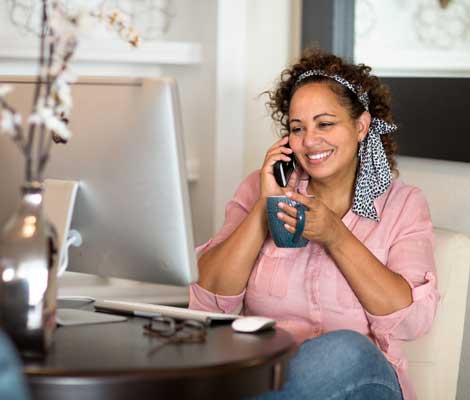 woman talks on the phone while working on the computer and drinking coffee